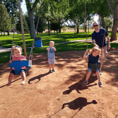 My daughters being pushed on swings by my husband and son at a park