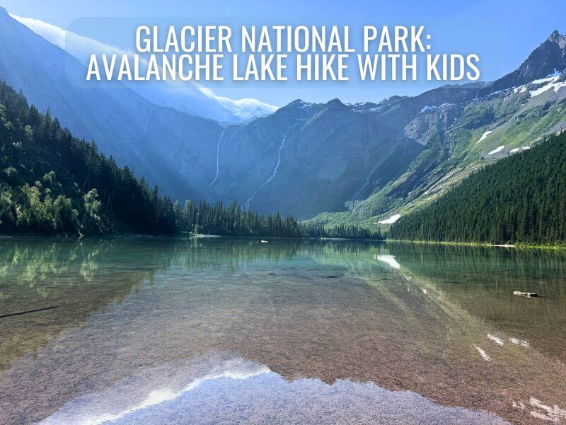 View of Avalanche Lake in Glacier National Park, surrounded by towering mountains with a clear, reflective lake in the foreground. Text overlay reads 'Glacier National Park: Avalanche Lake Hike with Kids.' Perfect spot for family hikes with stunning scenery.