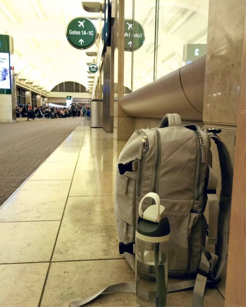 The very best personal item backpack in grey sitting on the floor of the John Wayne Airport next to my water bottle.